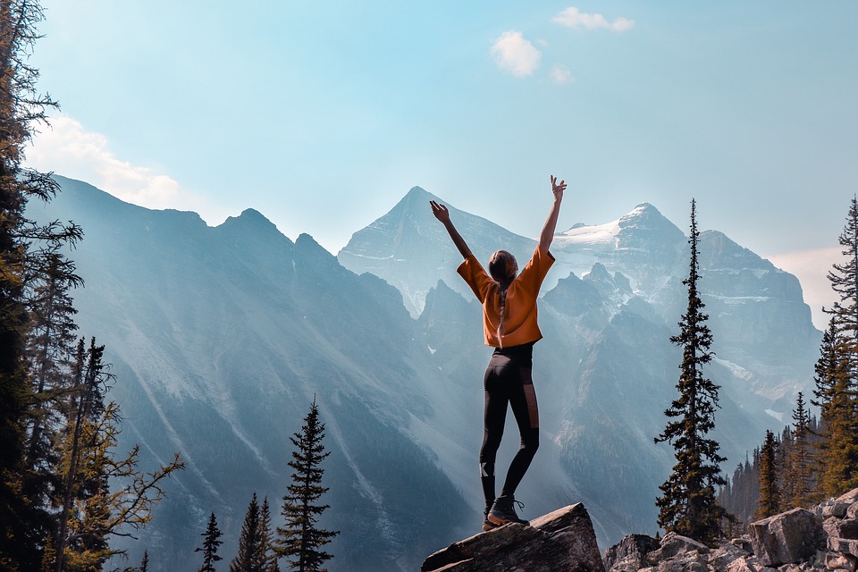 woman raises arms to celebrate achievements on summit of mountain