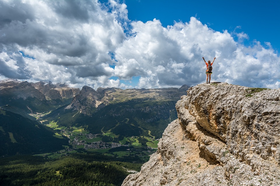 person on summit of mountain raises arms to celebrate achievement